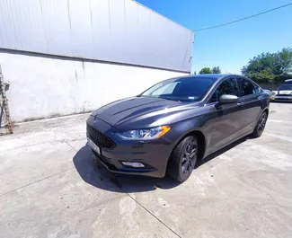 Vista frontal de um aluguel Ford Fusion Sedan no aeroporto de Kutaisi, Geórgia ✓ Carro #10702. ✓ Transmissão Automático TM ✓ 0 avaliações.